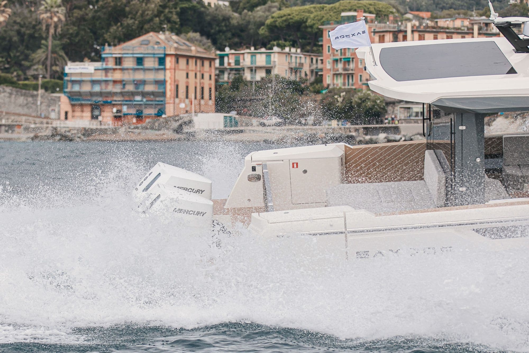 Twin Mercury outboards of the Saxdor 400 GTO throwing spray at speed off a harbor town